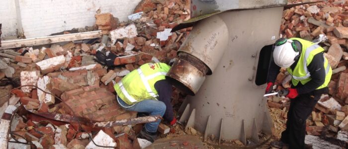 Two L A Moore Ltd operatives unbolt the base of the chimney prior to its demolition